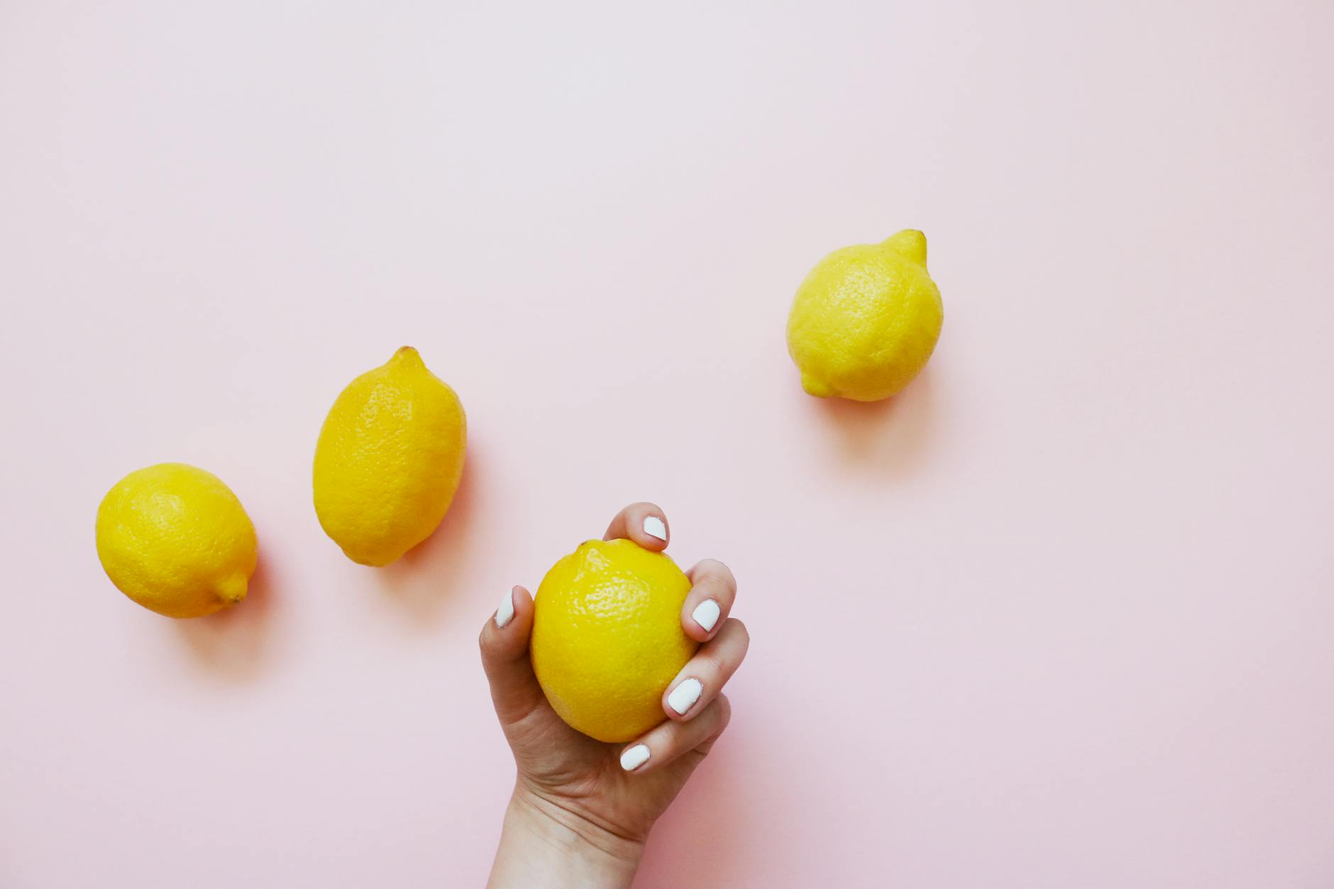 A hand holding a lemon on a soft pink background, symbolizing gentle self-care and recovery.