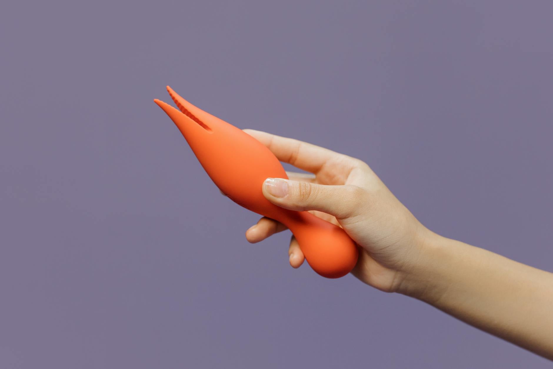 Hand holding a lemon clitoral vibrator against a minimalistic purple backdrop, showcasing modern sensuality and thoughtful pleasure exploration.